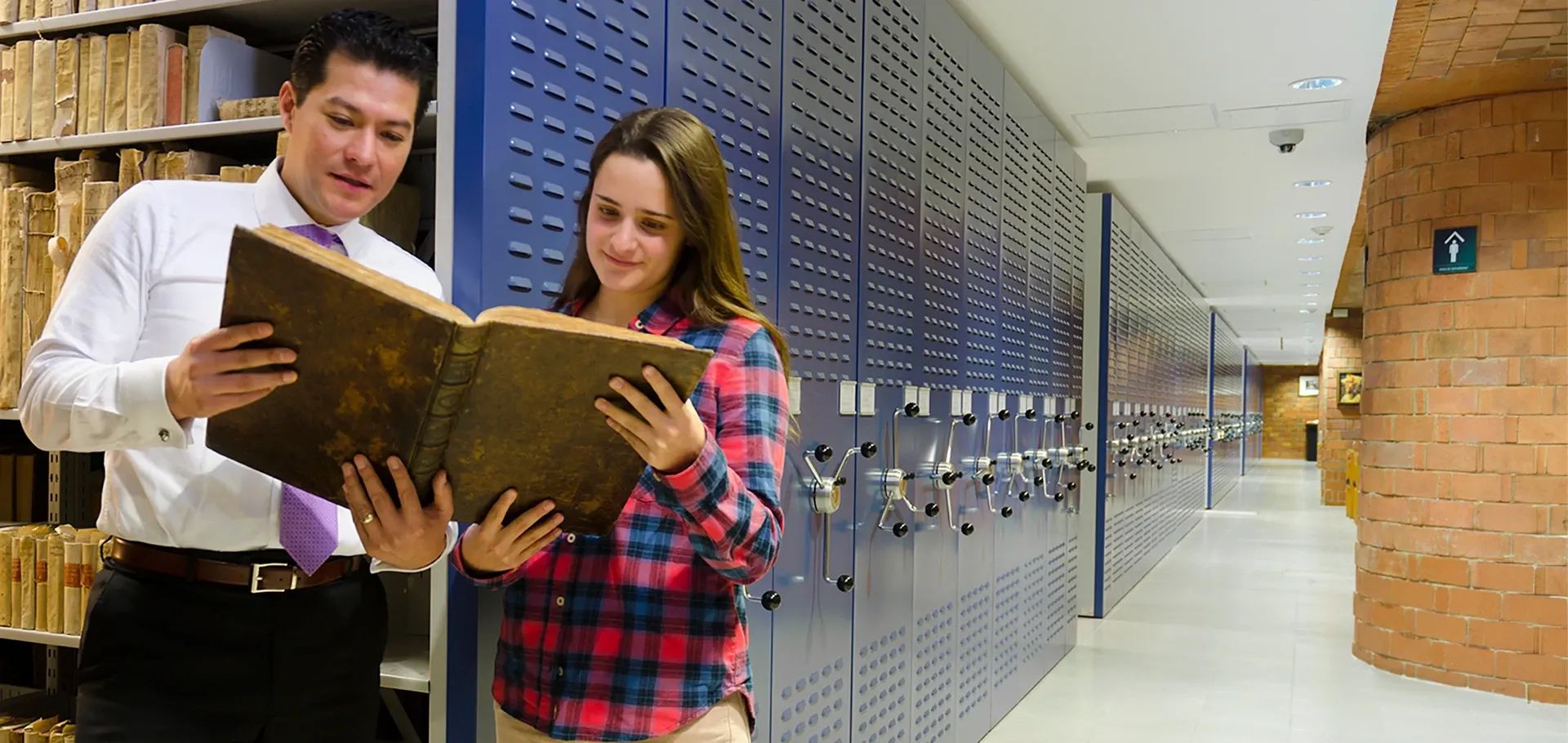 Estudiante y profesor viendo un libro en el acervo histórico de la Biblioteca Francisco Xavier Clavigero en la IBERO.